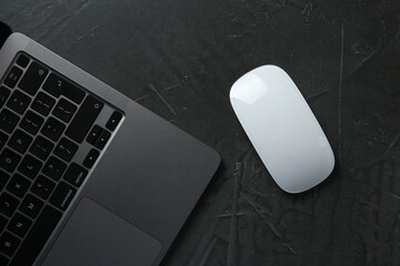 Wireless mouse and laptop on dark textured table, top view