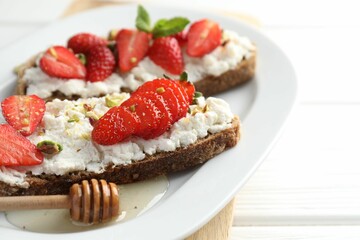 Delicious ricotta bruschettas with strawberry and pistachios served with honey on white table, closeup