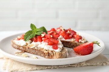 Bruschettas with ricotta cheese, chopped strawberries and mint on white wooden table, closeup