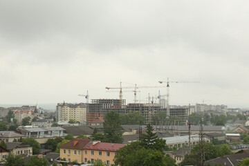 Picturesque view of city with buildings and construction cranes on cloudy day