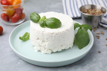 Fresh ricotta (cream cheese) and basil on gray table, closeup