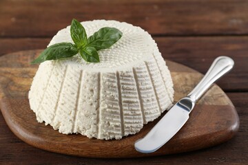 Tasty ricotta (cream cheese), basil and knife on wooden table, closeup