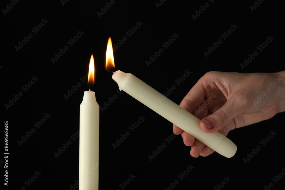 Wall mural woman lighting candle on black background, closeup