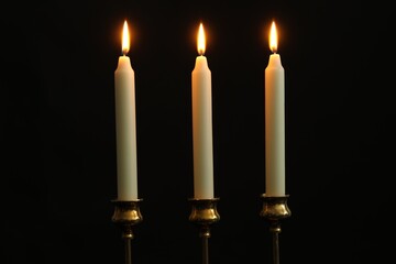 Many burning church candles on black background