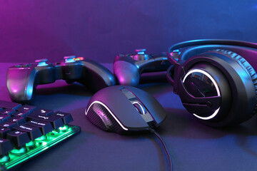 Computer mouse, headset, RGB keyboard and game controllers in neon lights on dark background, closeup © New Africa