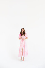 Model wearing casual outfit. Look in trendy minimalistic style. Pink dress with slit, belt, puff sleeves. Sexy sensual happy woman. Positive woman turn around and hold pink flower on white background.