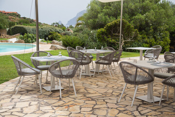 Garden and terrace design or landscaping: Natural stone terrace with tables and chairs and a beautiful view to the pool and the mountains in the Mediterranean Sea, Sardinia, Italy