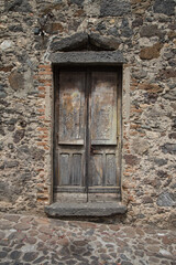 Old and weathered door of an medieval house built with stones, quarry stones and bricks along an alley with nature stone pavement in a village in Sardinia, Italy