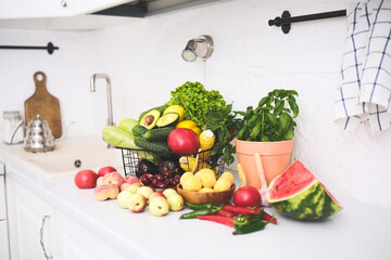 Fresh fruits, vegetables and greens on kitchen table in bright white kitchen, healthy lifestyle concept