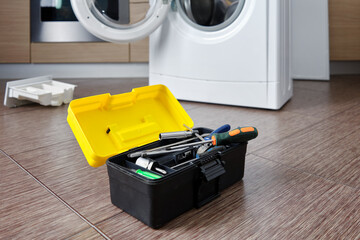 Close-up of a set of professional tools against the background of a disassembled washing machine in the kitchen. Professional repair of household appliances. Selective focus.