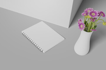 A realistic notebook mockup is lying on the floor close to the wall and there is a vase filled with beautiful flowers