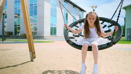 Smiling little girl riding on swing with net outdoors. Portrait of adorable caucasian child lying on net swing and playing in park