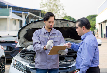 A mechanic in work uniform with gloves, holding document clipboard focused on the paperwork. The...