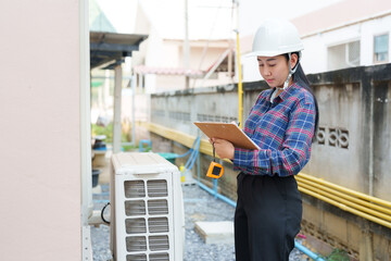 Asian female construction inspector reviewing air conditioning unit. Inspector wearing hard hat,...