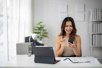 Fototapeta premium A woman is sitting at a desk with a laptop and a cell phone