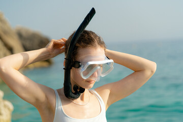 A young woman in a swimsuit puts a transparent mask with a snorkel on her face against the...