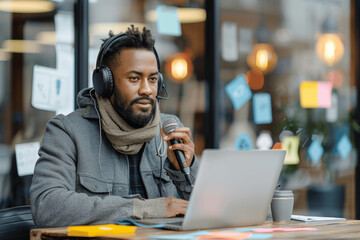 Obraz premium Young man in blue shirt with headphones at desk in modern office talking into microphone recording podcast with laptop during daylight