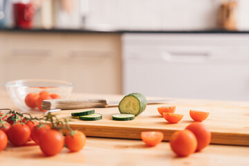 Slicing cherry tomatoes and cucumbers on a wooden table on a kitchen background.