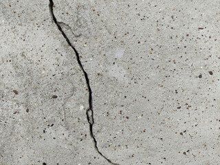 Cracked concrete surface covered with gray cement mortar. Destruction after the earthquake. Vertical uneven crack in the wall. Copy space.