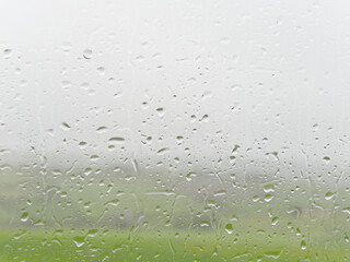 Droplets on a window obscure the view to a green landscape.
