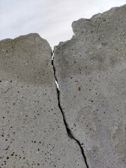 An old ruined, cracked, concrete wall of a building. Destruction after earthquake and precipitation. One deep, sinuous crack in a rough cement surface.