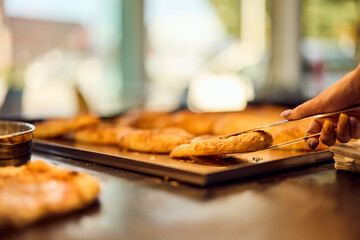 Photo of a female hand using kitchen tongs and holding pastry with cheese, at the bakery.