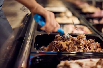A female uses an ice cream scooper and takes a scoop of chocolate ice cream.