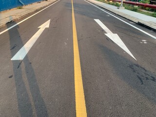 Asphalt Road with White Arrows and Yellow Line. A close-up view of white painted arrows on a grey asphalt road. The arrows indicate direction and guidance for vehicles.