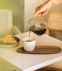 Woman's hand pouring coffee in a ceramic cup. Coffee shop table. Coffee concept