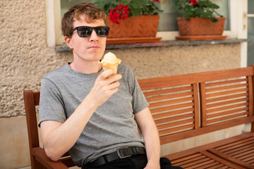 Young Male Model Enjoying Ice Cream on a Sunny Day, Sitting on a Bench