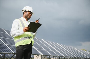 African male engineer inspects solar panels and uses walkie-talkie