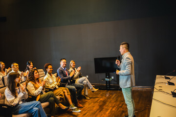 Male Asian CEO having speech on press conference in convention center. Group of multiracial colleagues listening.