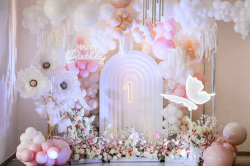 Arch decorated pink, white balloons, text Happy Birthday, flowers, paper decor butterfly. Birthday party for 1 year old girl on a background photo wall. Children's photo zone.