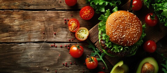 Top view of a burger with avocado, lettuce, and cherry tomatoes on a wooden surface, offering copy space in the image.