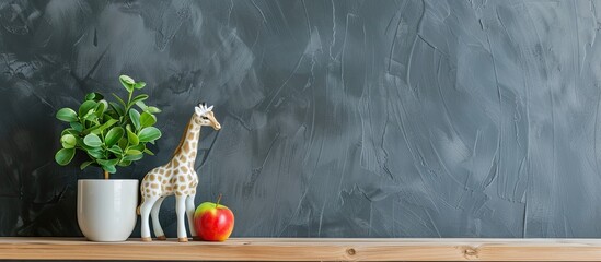 Decorative giraffe figurine, potted plant, and apples on wooden shelf against grey wall, copy space image.
