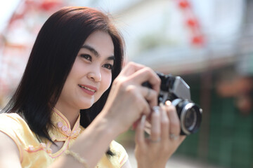 A portrait of pretty woman in yellow chinese traditional costume taking a photo by using her vintage film camera in the Chinese new year celebration.