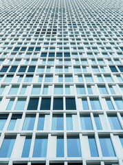 facade of a modern high-rise building, characterized by a grid of windows and frames. The structure is tall, with a repeating pattern of glass panes reflecting the sky