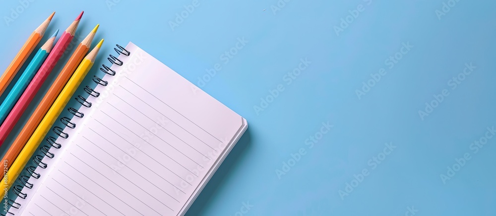 Aufkleber a bird's eye view of an open notepad and colorful pencils on a blue backdrop, providing ample copy s