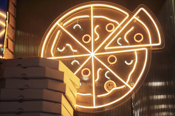 Pizza logo, brand name. Neon pizza sign, bright design, light banner. A lot of cardboard boxes on the background of a sign on the wall with space for copying. Pizza Delivery Concept.High quality photo