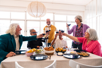Group of happy senior friends bonding at home for dinner party - Cheerful and youthful old mature multiethnic people having fun