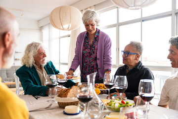 Group of happy senior friends bonding at home for dinner party - Cheerful and youthful old mature multiethnic people having fun