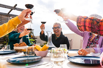 Group of happy senior friends bonding at home for dinner party - Cheerful and youthful old mature multiethnic people having fun and dining on a rooftop terrace 
