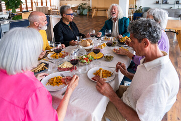 Group of happy senior friends bonding at home for dinner party - Cheerful and youthful old mature multiethnic people having fun