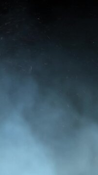 Vertical Blue Smoke and Ash Rolling 4K Loop features blue hued smoke and ash or snow rolling from left to right against a black background in a vertical ratio loop.