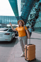 Happy traveling Caucasian woman tourist passenger is using mobile application to call pick up taxi at airport terminal for transportation during her vacation travel and long weekend holiday. High