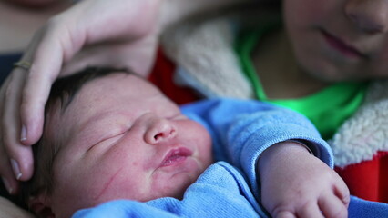 Young sibling gazes adoringly at newborn baby while sitting next to their mother, showcasing a...