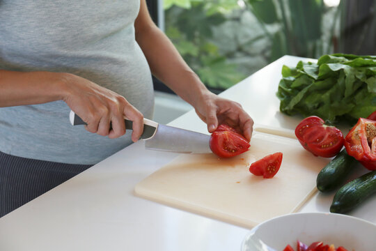 Cropped shot of a pregnant woman on a third trimester cooking a healthy plant based meal on a white marble countertop. Close up, copy space, background.