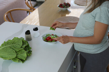 Cropped shot of a pregnant woman on a third trimester cooking a salad using fresh organic ingredients. Expecting mother preparing a healthy snack. Close up, copy space, background.