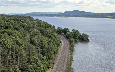 view of train tracks next to river from kingston rhinebeck bridge in hudson valley (railroad line near water near mountains) curve in track turning trains looking down new york state transport commute