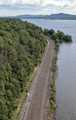 view of train tracks next to river from kingston rhinebeck bridge in hudson valley (railroad line near water near mountains) curve in track turning trains looking down new york state transport commute